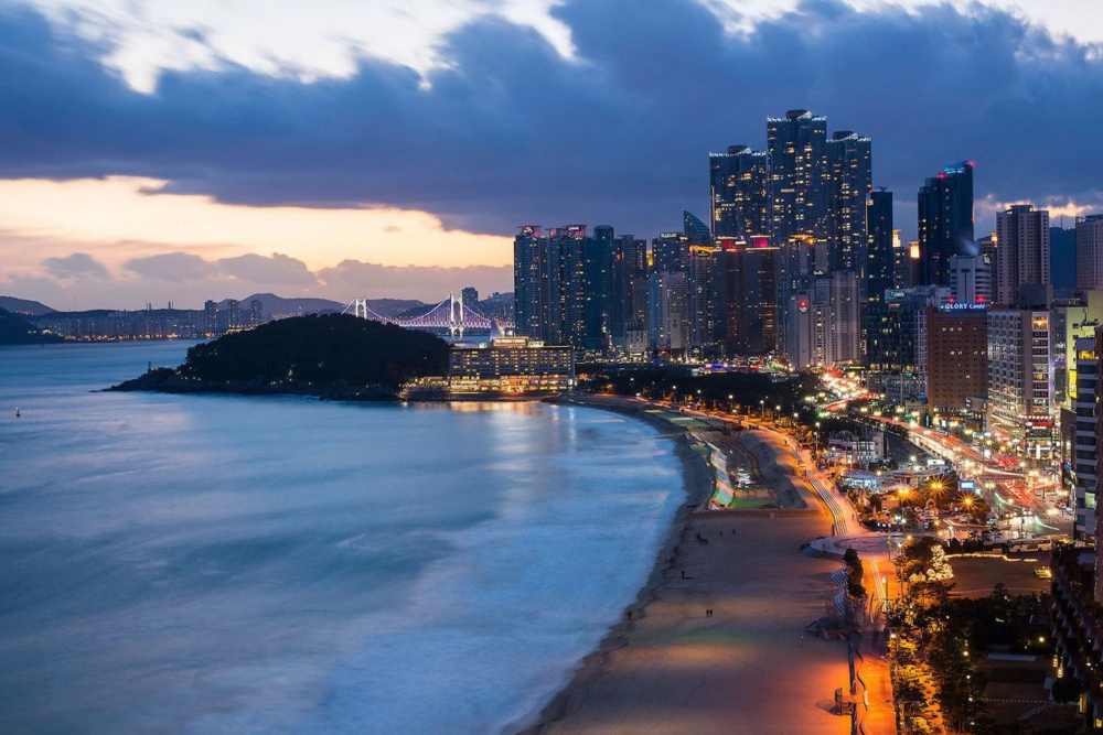 Khám phá những bãi biển đẹp nhất châu Á Haeundae là một bãi biển nằm trên địa phận quận Haeundae-gu, tỉnh Busan, Hàn Quốc, có đường bờ biển dài khoảng 12km với diện tích hơn 58 nghìn m2. Khi đặt chân đến Haeundae, bạn sẽ choáng ngợp trước khung cảnh thiên nhiên hùng vĩ – bờ cát trắng mịn trải dài tựa như dải lụa uốn lượn, ôm lấy làn nước biển xanh ngọc bích lấp lánh dưới ánh mặt trời. Bầu không khí nơi đây rất trong lành và mát mẻ, có thể xua tan đi mọi muộn phiền, lo âu của cuộc sống thường nhật. Đặc biệt, Haeundae còn nổi tiếng với các lễ hội diễn ra quanh năm, từ lễ hội pháo hoa Busan, lễ hội cát Haeundae, lễ hội cá trích Busan… là những sự kiện không thể bỏ qua khi đến với bãi biển đẹp nhất Hàn Quốc này. Với vẻ đẹp thiên nhiên say đắm lòng người, cùng vô số hoạt động vui chơi giải trí và ẩm thực phong phú, Haeundae xứng đáng là điểm đến lý tưởng cho du khách trong và ngoài nước.